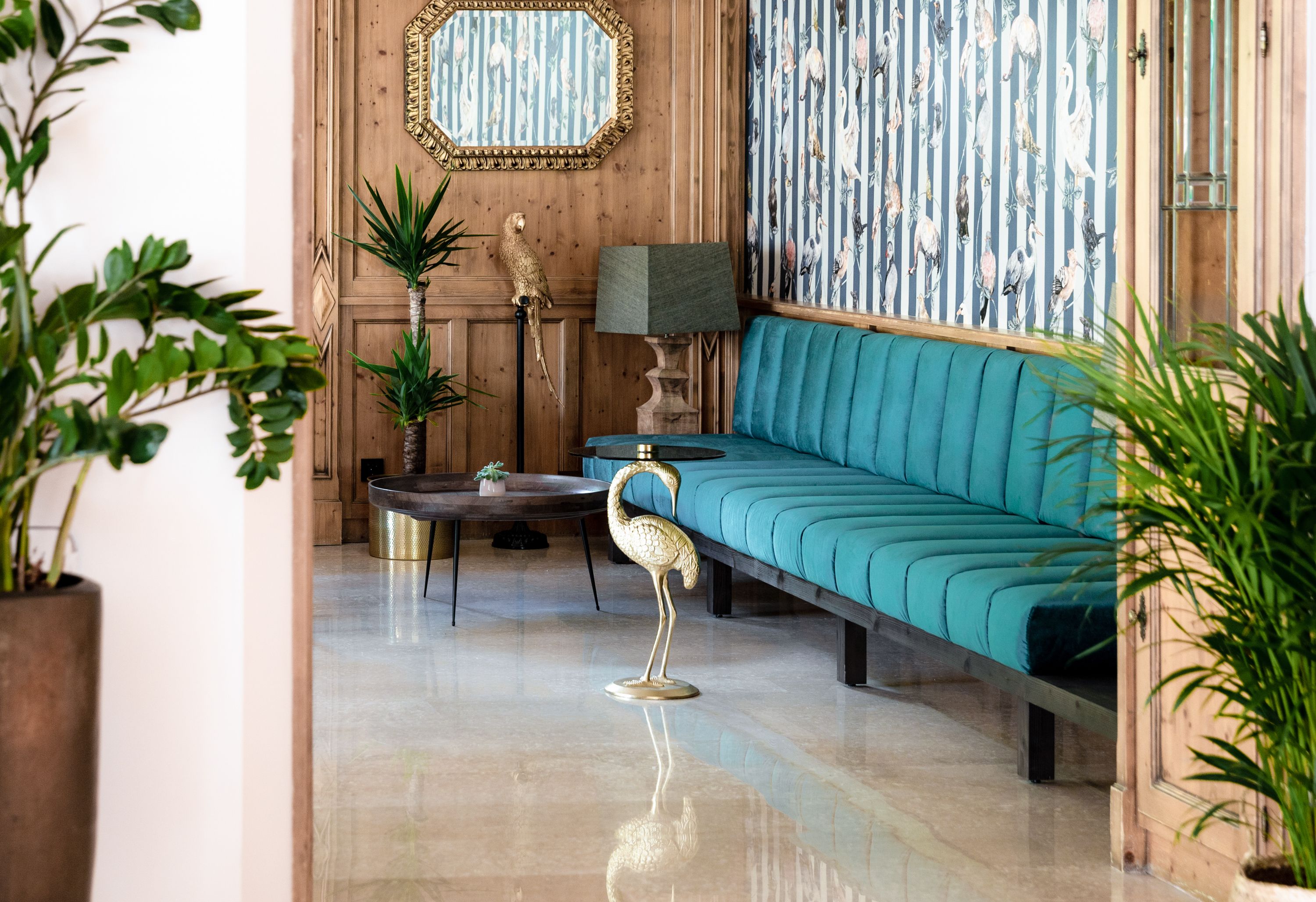 A room with a teal sofa, a wooden wall with a mirror, a patterned wallpaper, and a floor lamp.