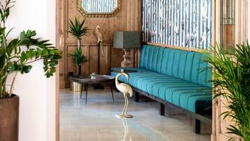 A room with a teal sofa, a wooden wall with a mirror, a patterned wallpaper, and a floor lamp.