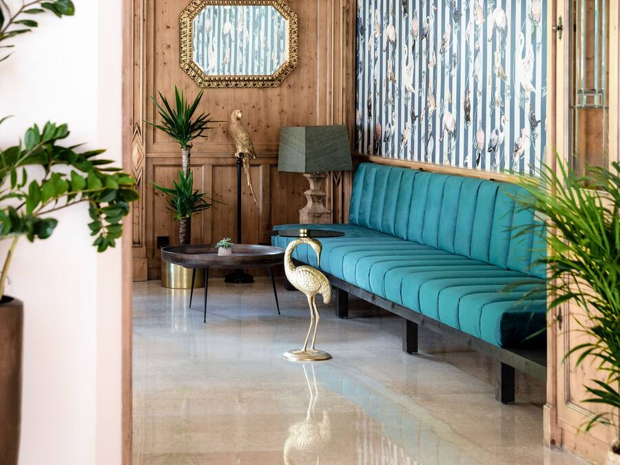 A room with a teal sofa, a wooden wall with a mirror, a patterned wallpaper, and a floor lamp.