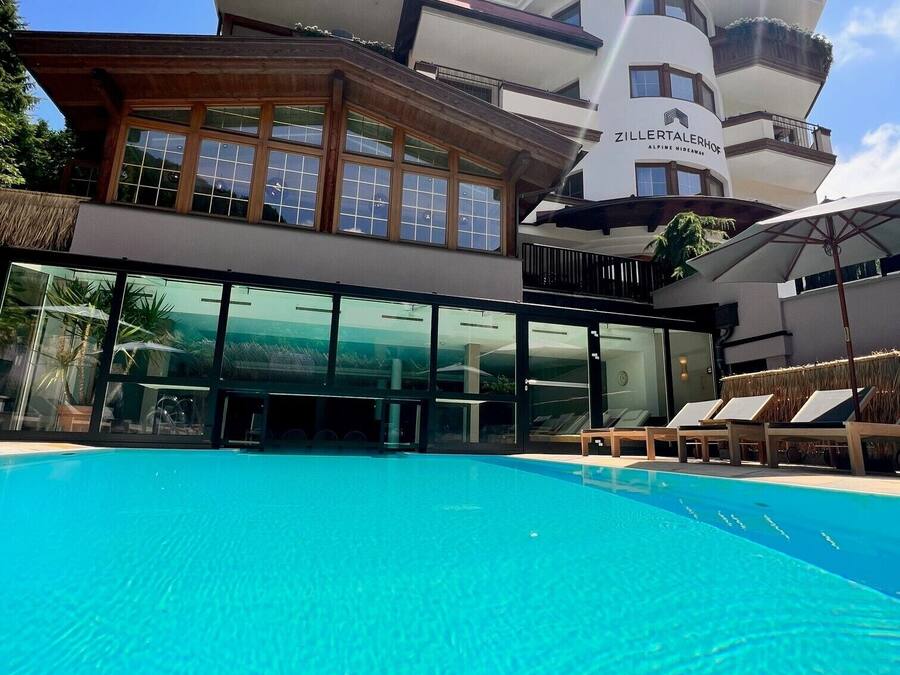 Un hôtel moderne doté d’une grande piscine, d’une façade en verre et d’une enseigne indiquant « Zillertalerhof, un havre de paix en montagne ».