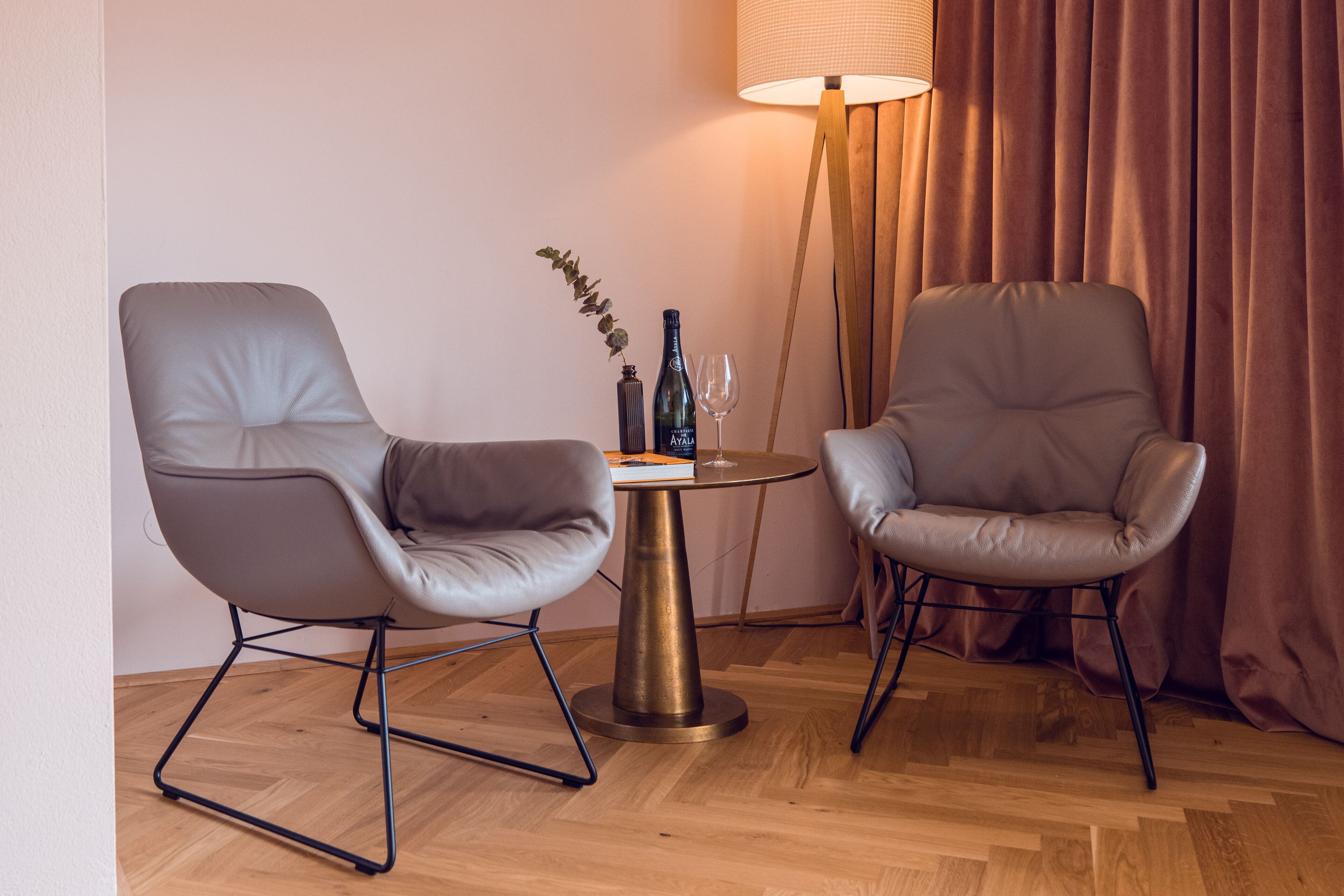 Two leather chairs, a small round table with a lamp, and a bottle and glass on the table.