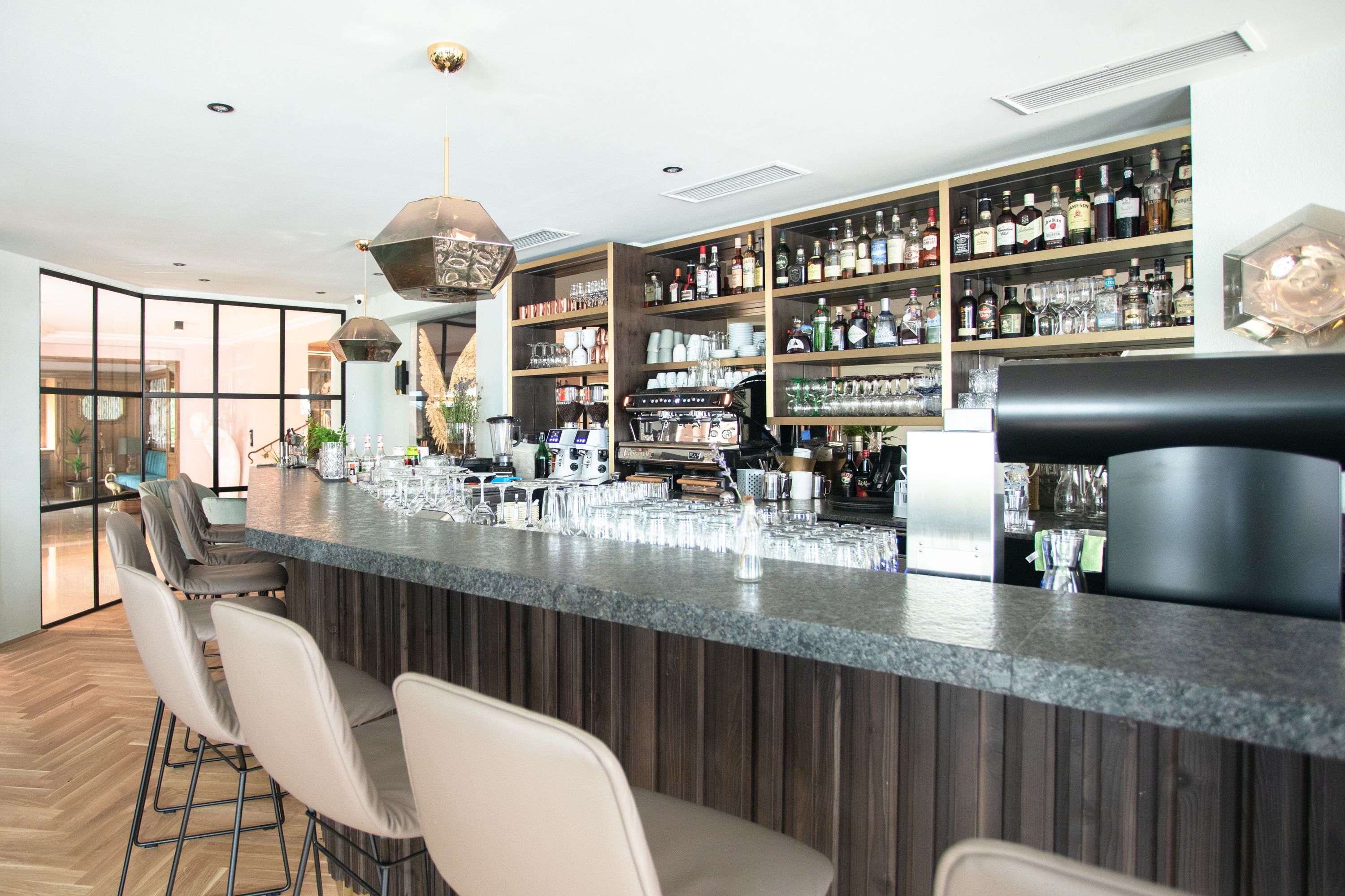 A modern bar area with a long counter, bar stools, and shelves stocked with liquor bottles.