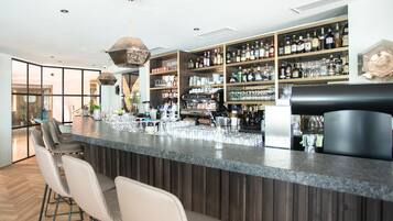 A modern bar area with a long counter, bar stools, and shelves stocked with liquor bottles.