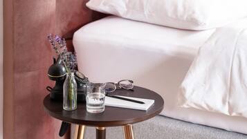 A small round table with a dark wood finish and gold legs, placed on a carpeted floor. On the table, there is a clear glass of water, a black vase with purple flowers, a pair of glasses, and a white notepad with a pen.