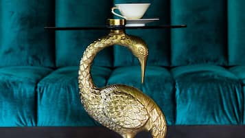 Una escultura dorada con forma de pájaro sobre un pedestal, una taza y platillo blancos encima, y un sofá tapizado color aguamarina al fondo.