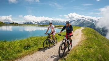 Dos ciclistas en un camino de grava junto a un lago, con montañas al fondo.