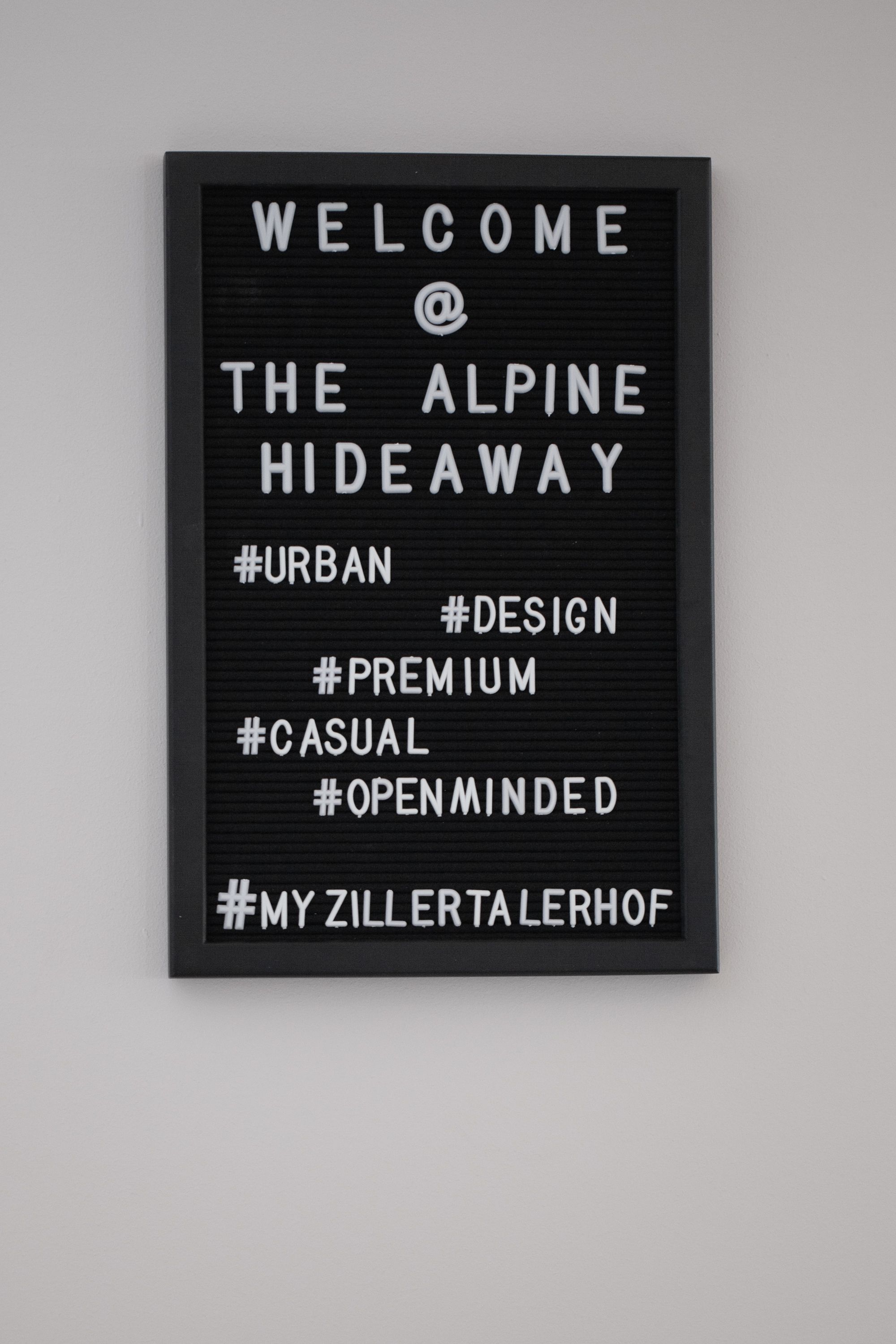 A framed welcome sign with the text "WELCOME @ THE ALPINE HIDEAWAY" and hashtags like #URBAN, #DESIGN, #PREMIUM, #CASUAL, #OPENMINDED, #MY ZILLERTALERHOF.