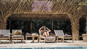 Un espace aménagé au bord de la piscine, avec des chaises longues, une structure dotée d’un toit de chaume et un panneau indiquant : « La vie est une montagne, pas une plage. »