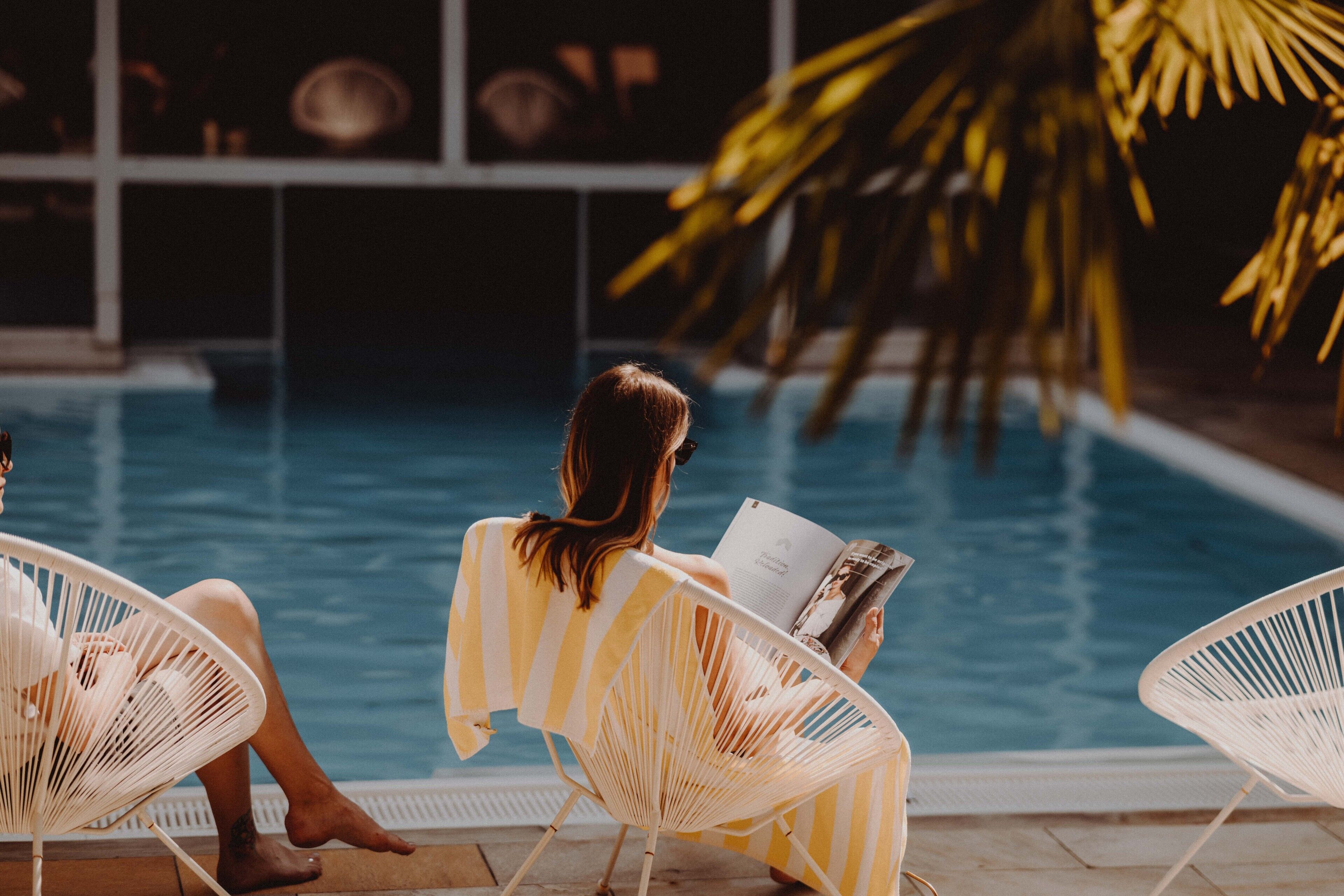 Zona de piscina con sillas de descanso y una persona leyendo un libro.