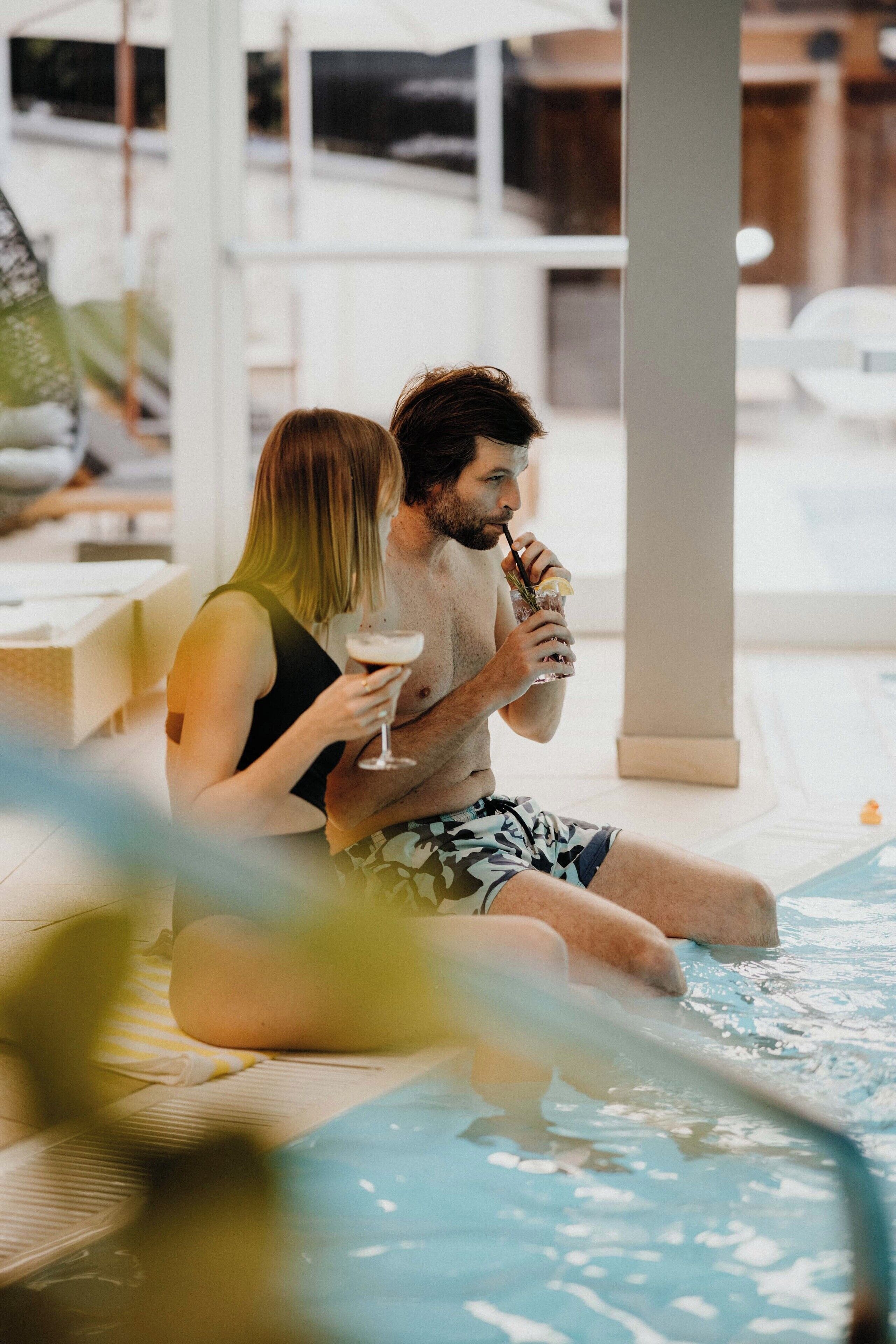 Ein Paar sitzt am Pool und hält Getränke.