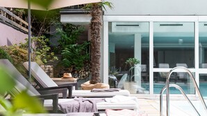 Un espace aménagé au bord de la piscine, avec des chaises longues, un palmier et une porte vitrée donnant accès à la piscine.