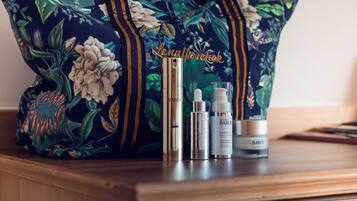 A floral-patterned bag, a gold-colored bottle, and two skincare containers on a wooden surface.