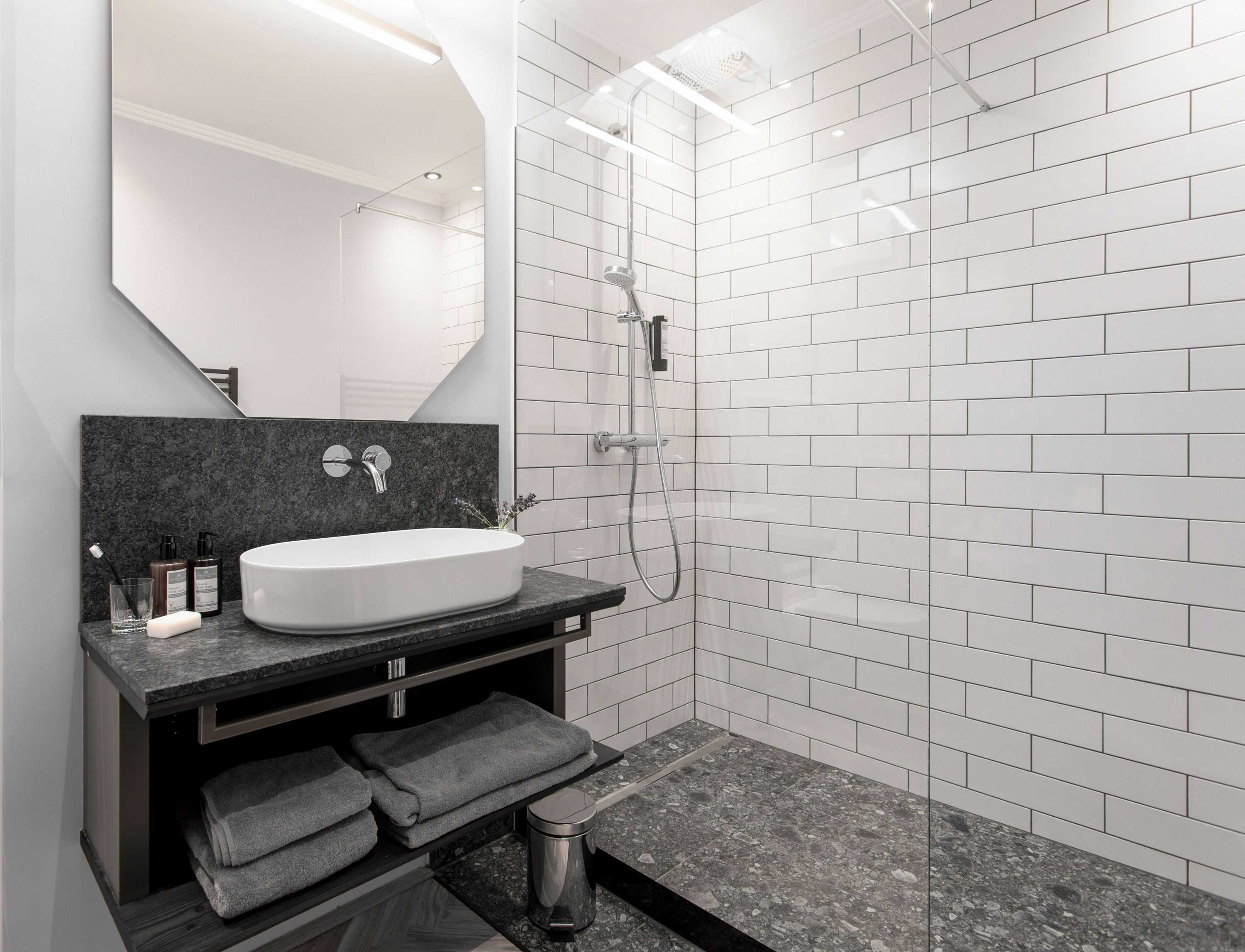 A modern bathroom with a white sink, dark granite countertop, and a glass shower enclosure.