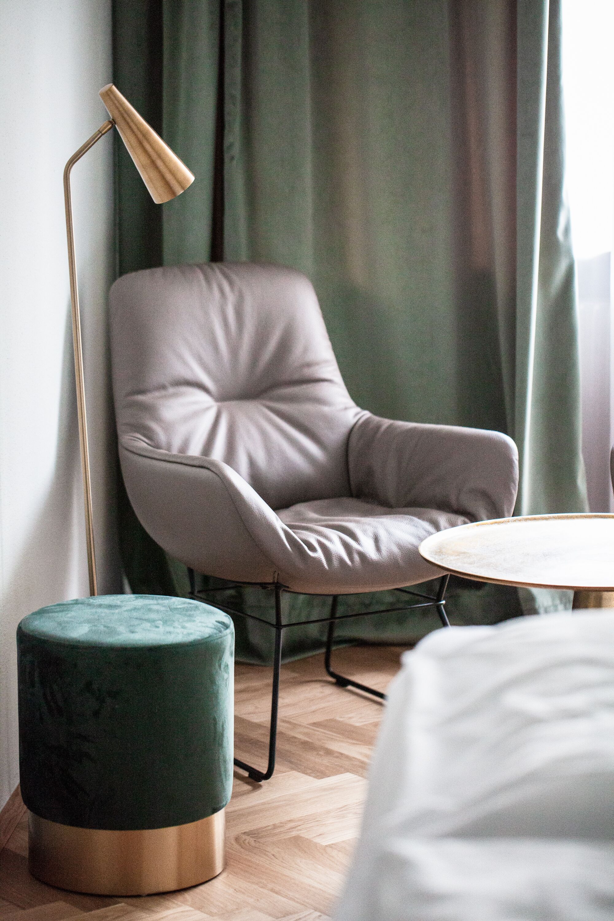 Una habitación moderna con un sillón tapizado de color gris, una mesa redonda y un otomano verde.