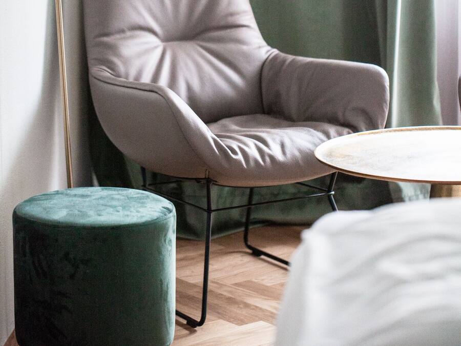 Una habitación moderna con un sillón tapizado de color gris, una mesa redonda y un otomano verde.