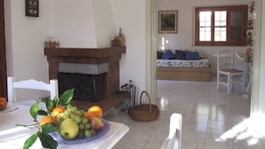 A living room with a fireplace, a dining table with fruit, a sofa, and a window with curtains. - Apartment- Rosa 4+2 - Two Bedroom Apartment, Sleeps 6 (Val Canina)