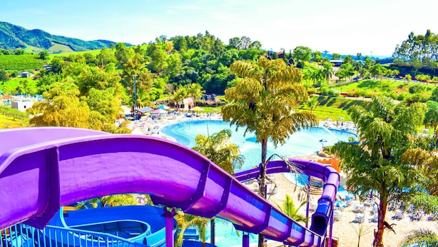 Ein Wasserpark mit einer großen, violetten Rutsche, einem Pool und einem Strandbereich.