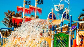 Ein Wasserspielbereich mit einer großen Rutsche, mehreren Flaggen und einem Spritzschutz.