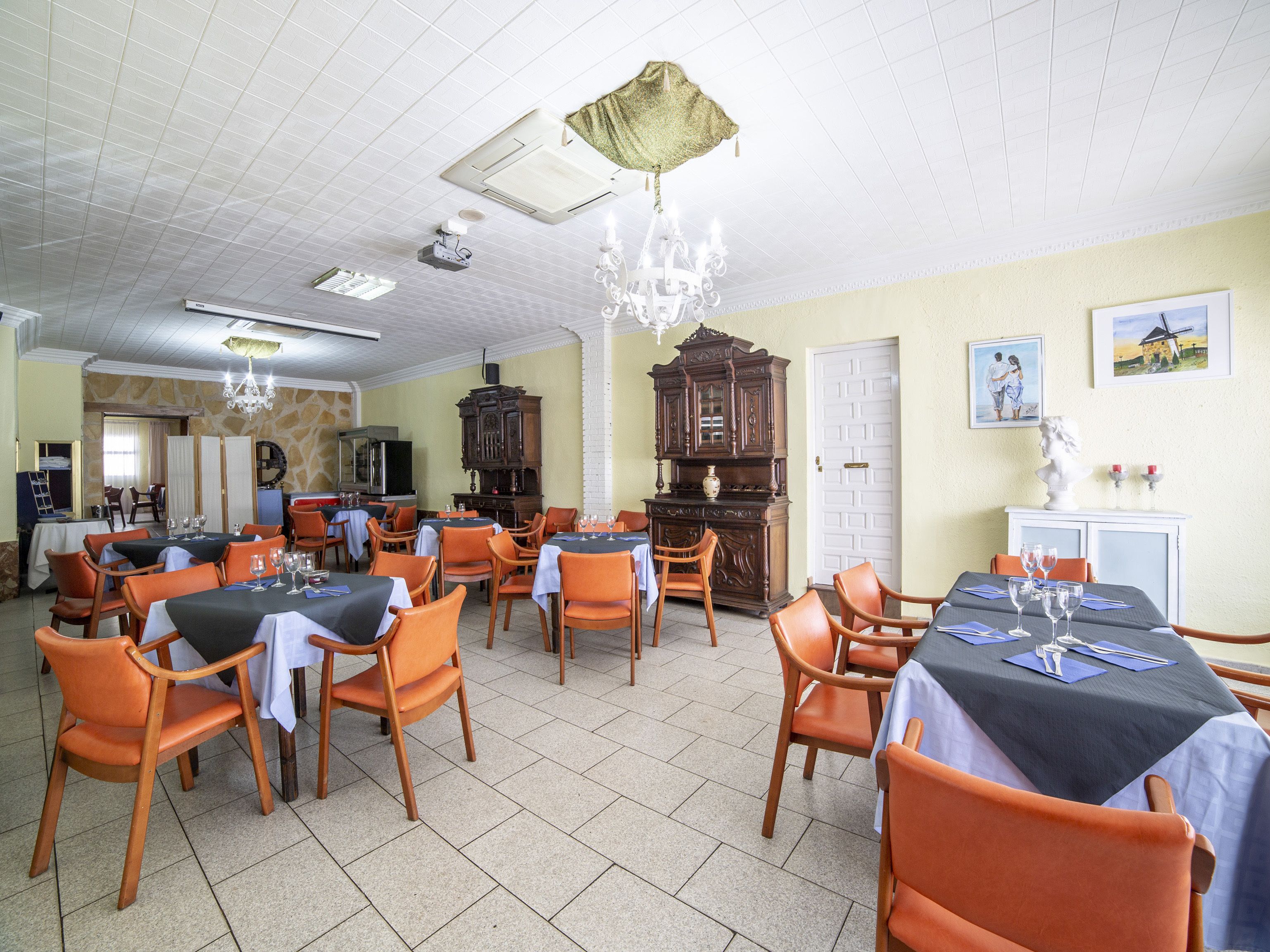 Un espace repas avec des tables et des chaises, un lustre et un grand buffet en bois.