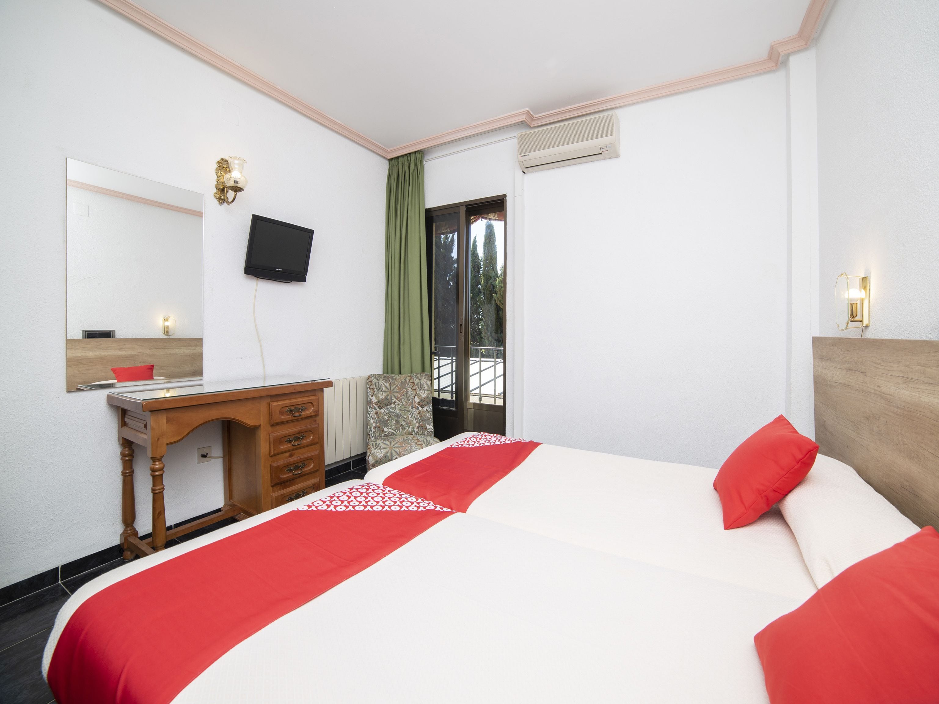 Habitació d'hotel amb un llit, escriptori, cadira, televisió i finestra amb vista a arbres.