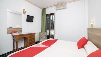 Habitació d'hotel amb un llit, escriptori, cadira, televisió i finestra amb vista a arbres.