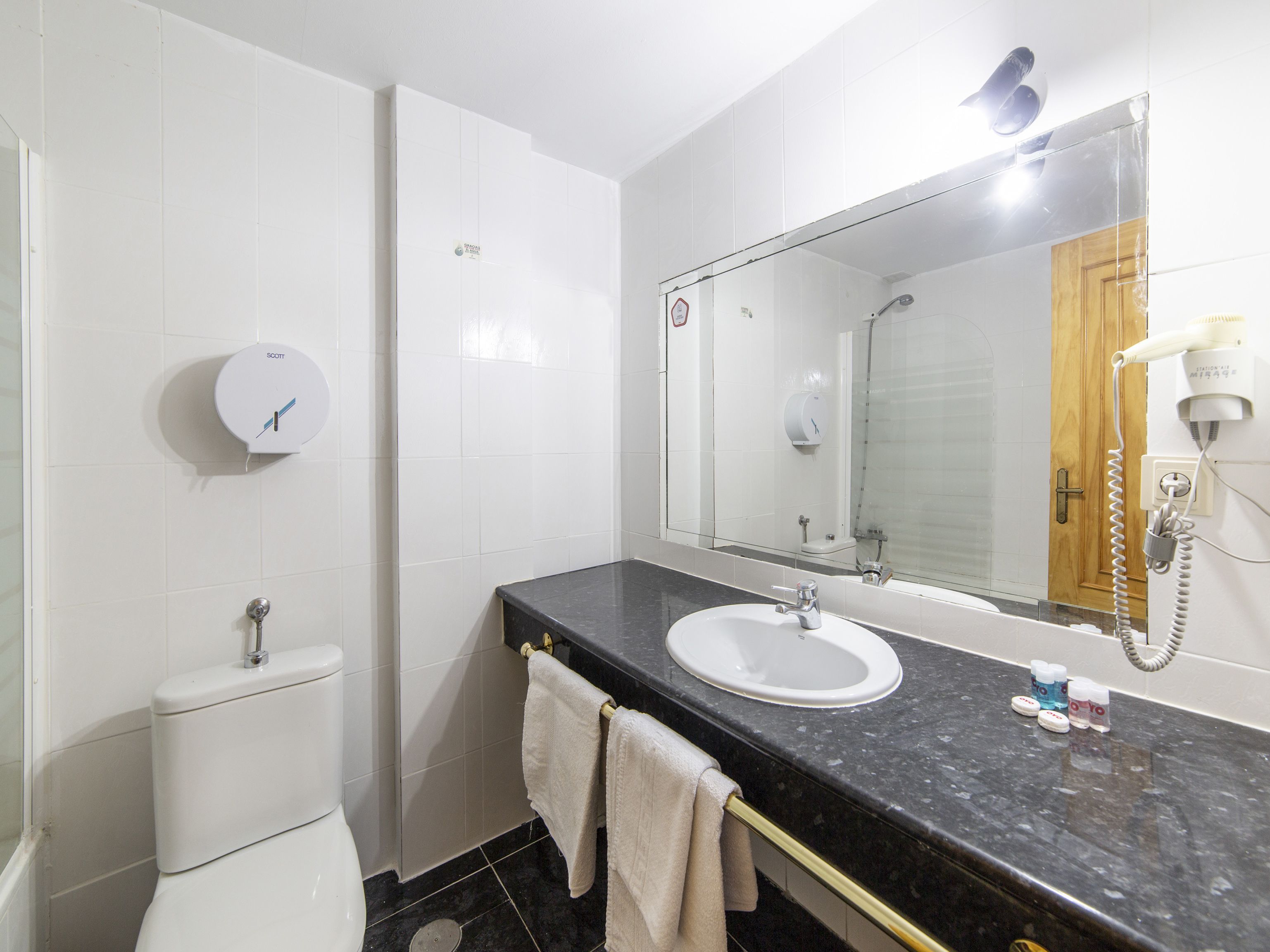 Une salle de bain avec des toilettes blanches, un lavabo avec un miroir au-dessus et un porte-serviettes.