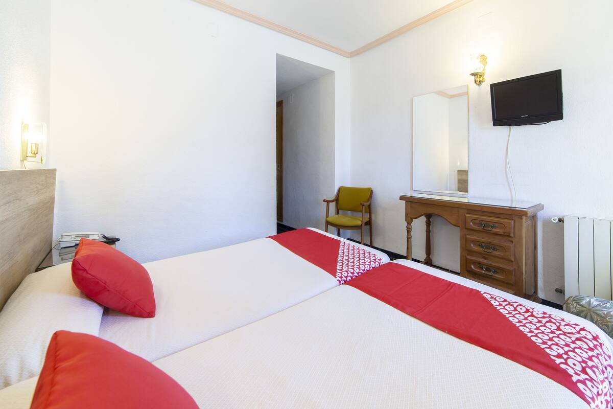 Habitación de hotel con cama, cómoda de madera, una silla, televisor y espejo.
