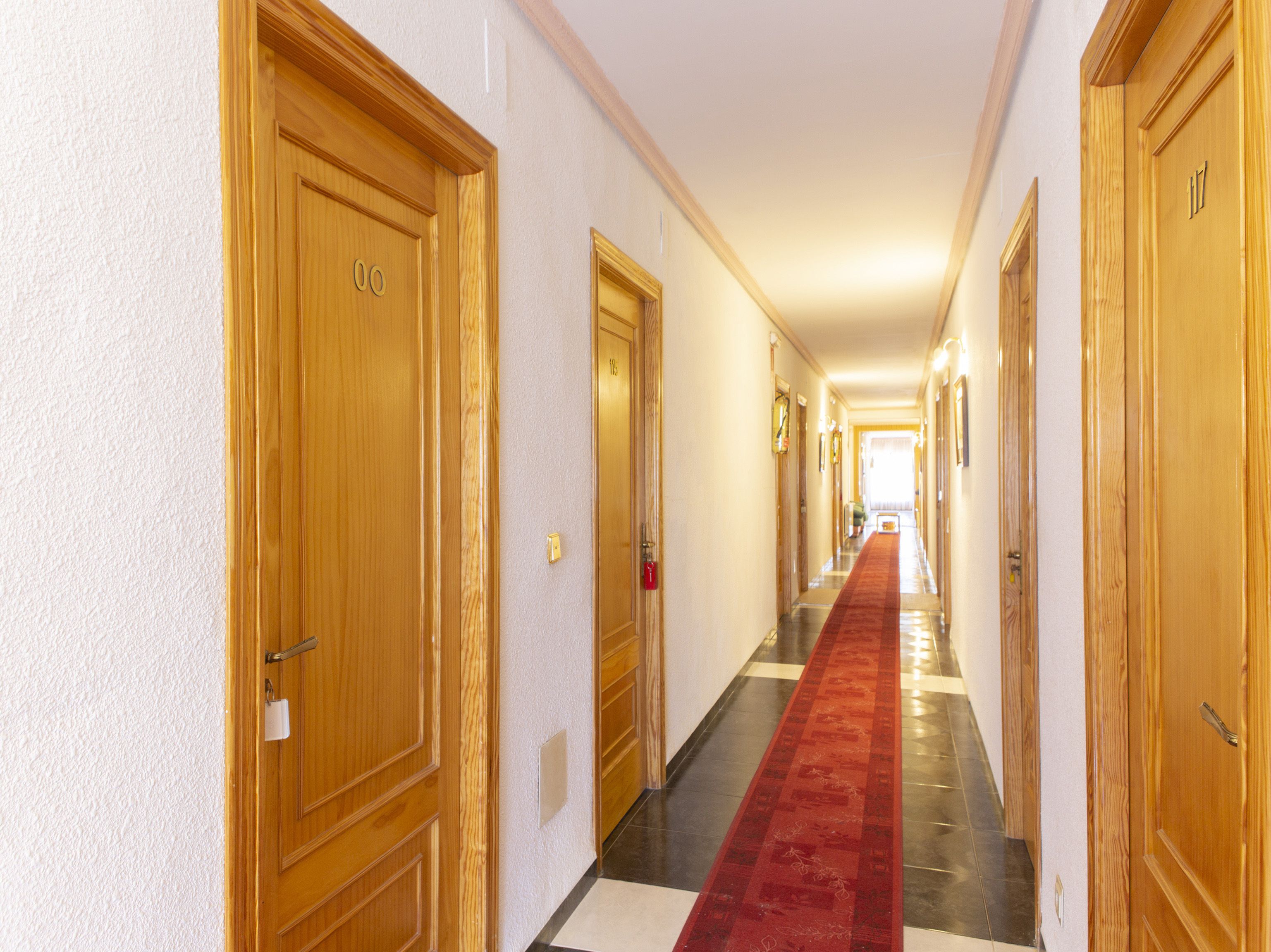 A hotel hallway with wooden doors, a red carpet, and a checkered floor.