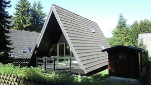 A modern, triangular-roofed building with a wooden deck and a small shed. - Holiday park- Nurdach (Clausthal)