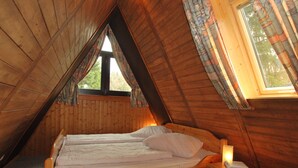 A wooden cabin bedroom with a bed, a nightstand, and a window with curtains. - Holiday park- Nurdach (Clausthal)