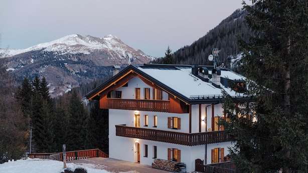 A two-story lodge with a wooden facade, multiple balconies, and a snow-covered mountain in the background. - Sas Ciapel with private bio sauna (Livinallongo del col di lana)