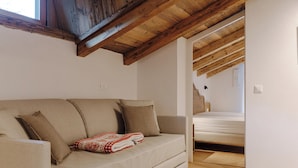 A cozy room with a sofa, a bed, wooden beams, and a window. - Sas Ciapel with private bio sauna (Livinallongo del col di lana)