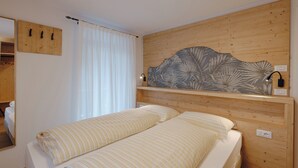 A bedroom with a wooden headboard, a bed with striped bedding, a mirror, and a wall-mounted shelf with a decorative piece. - Aurone with private bio sauna (Livinallongo del col di lana)