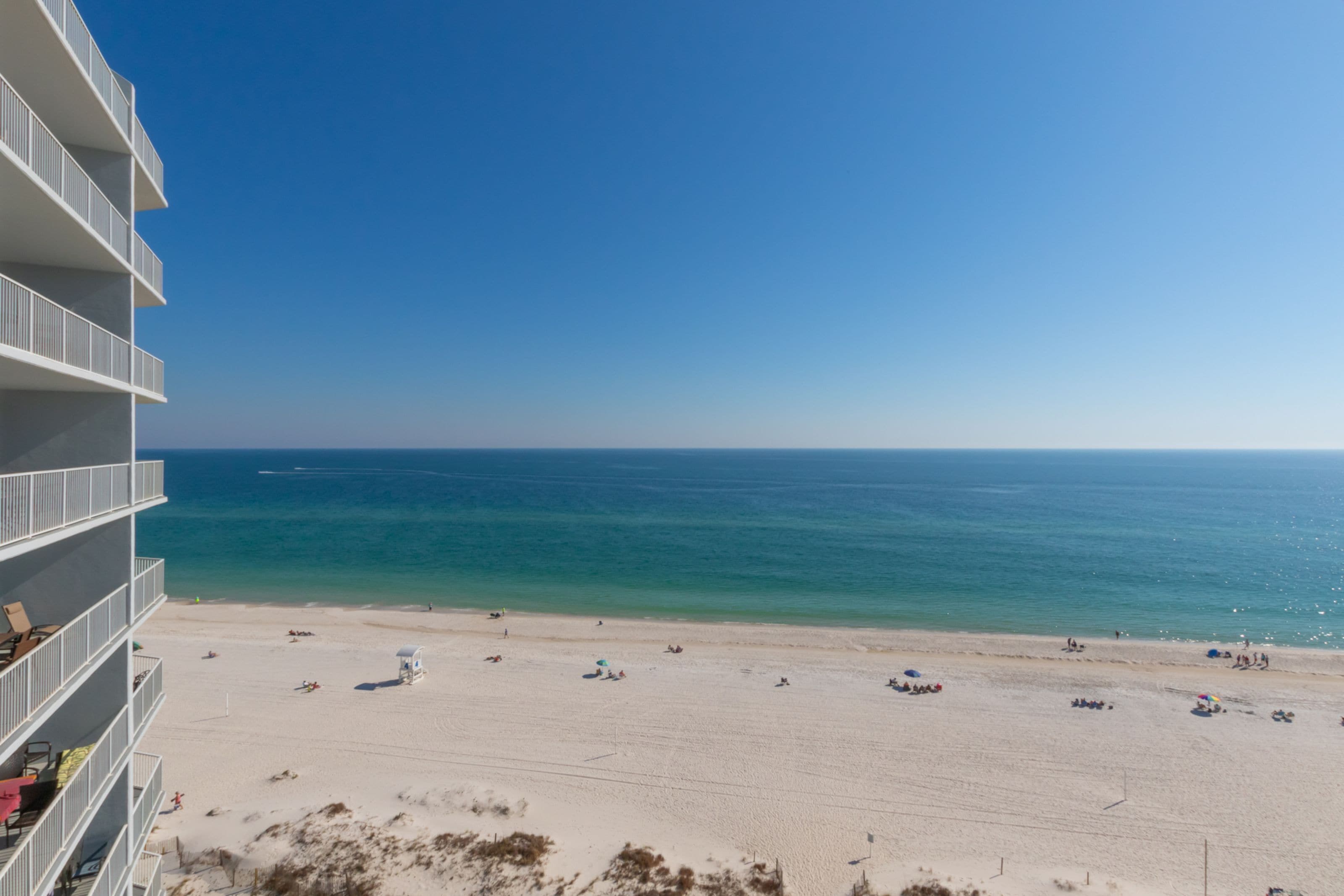 A beach view from a hotel balcony with a clear sky, sandy beach, and ocean.