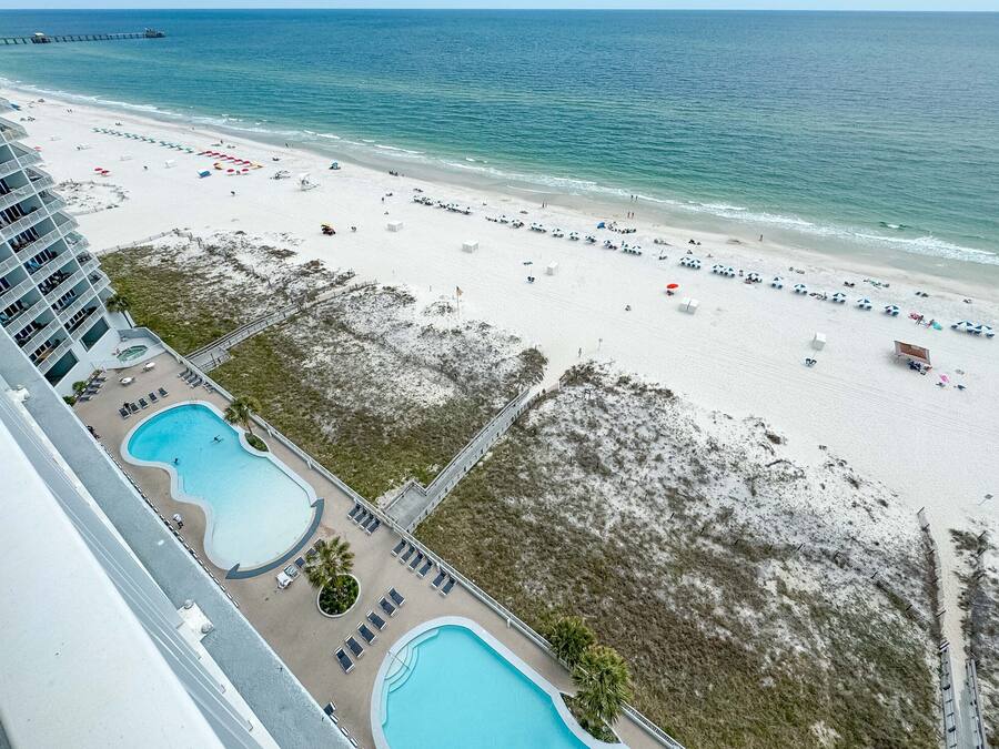 A beach resort with a pool area, beach umbrellas, and a pier in the background.