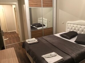 A bedroom with a bed, a mirror, and a wooden floor.