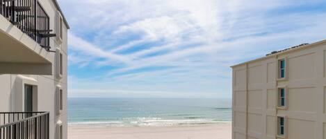 A beachfront view from a balcony overlooking a sandy beach and ocean.