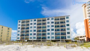 A multi-story hotel with balconies, located on a sandy beachfront with a clear sky. - Island Sunrise Condos by Hosteeva (Gulf Shores)
