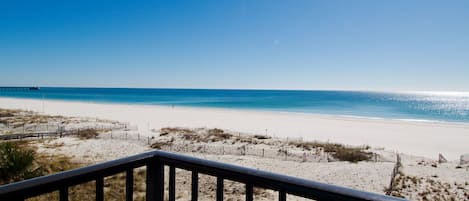 A beach view from a balcony with a railing, sandy beach, and ocean.
