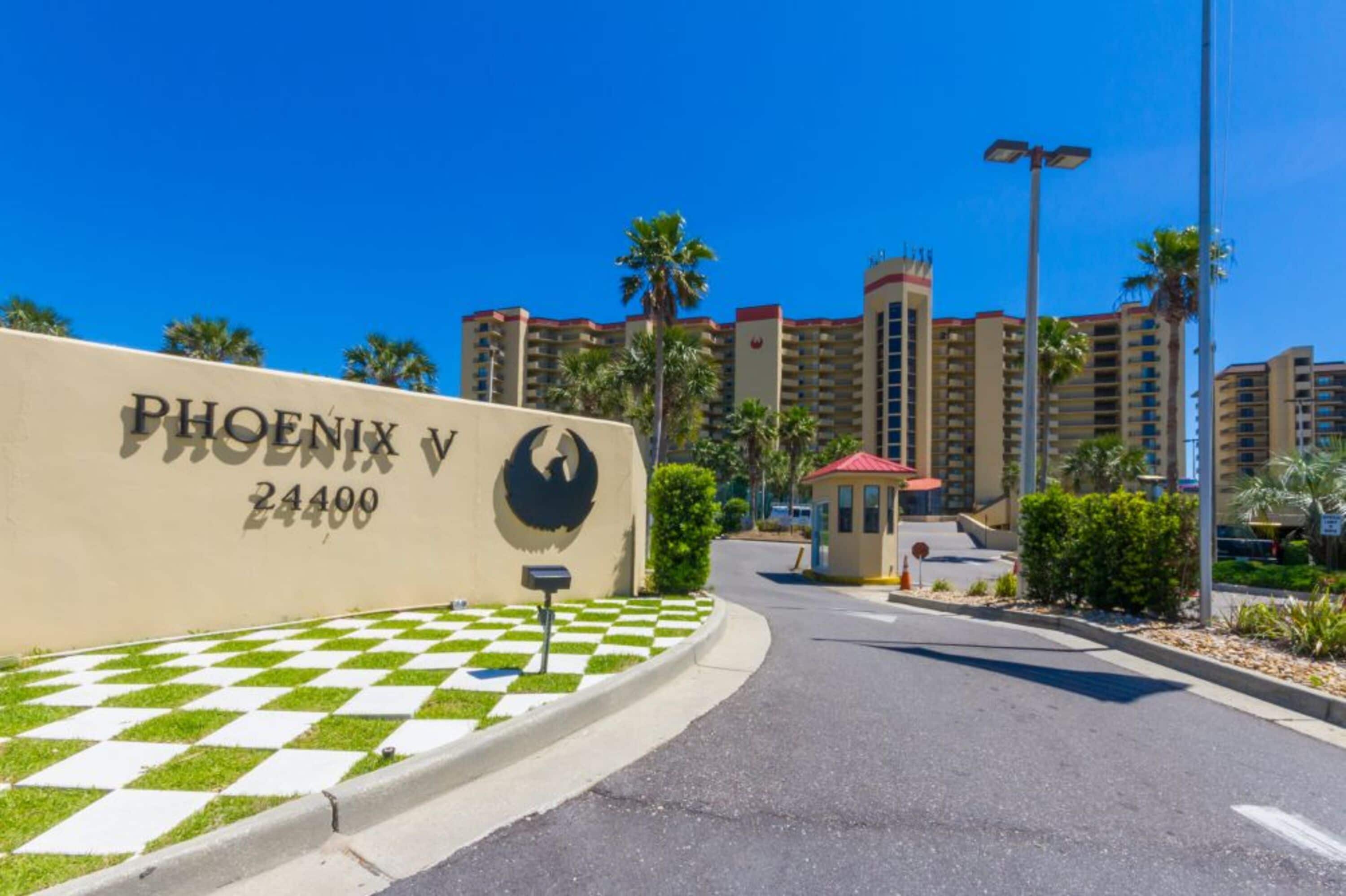 A hotel entrance with a checkered pavement, a large building with a red roof, and palm trees in the background.