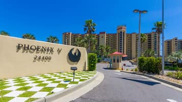 A hotel entrance with a checkered pavement, a large building with a red roof, and palm trees in the background.