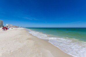 A beach with a clear sky, sandy shore, and buildings in the background. - Phoenix V 202 (Orange Beach)