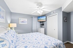 Ein Schlafzimmer mit einem Bett, einem Deckenventilator, einem Fernseher und einer Tür.