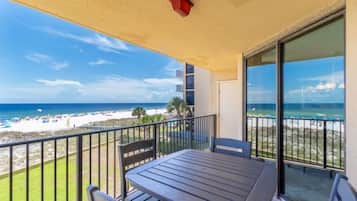 A balcony with a table and chairs, overlooking a beach and ocean.