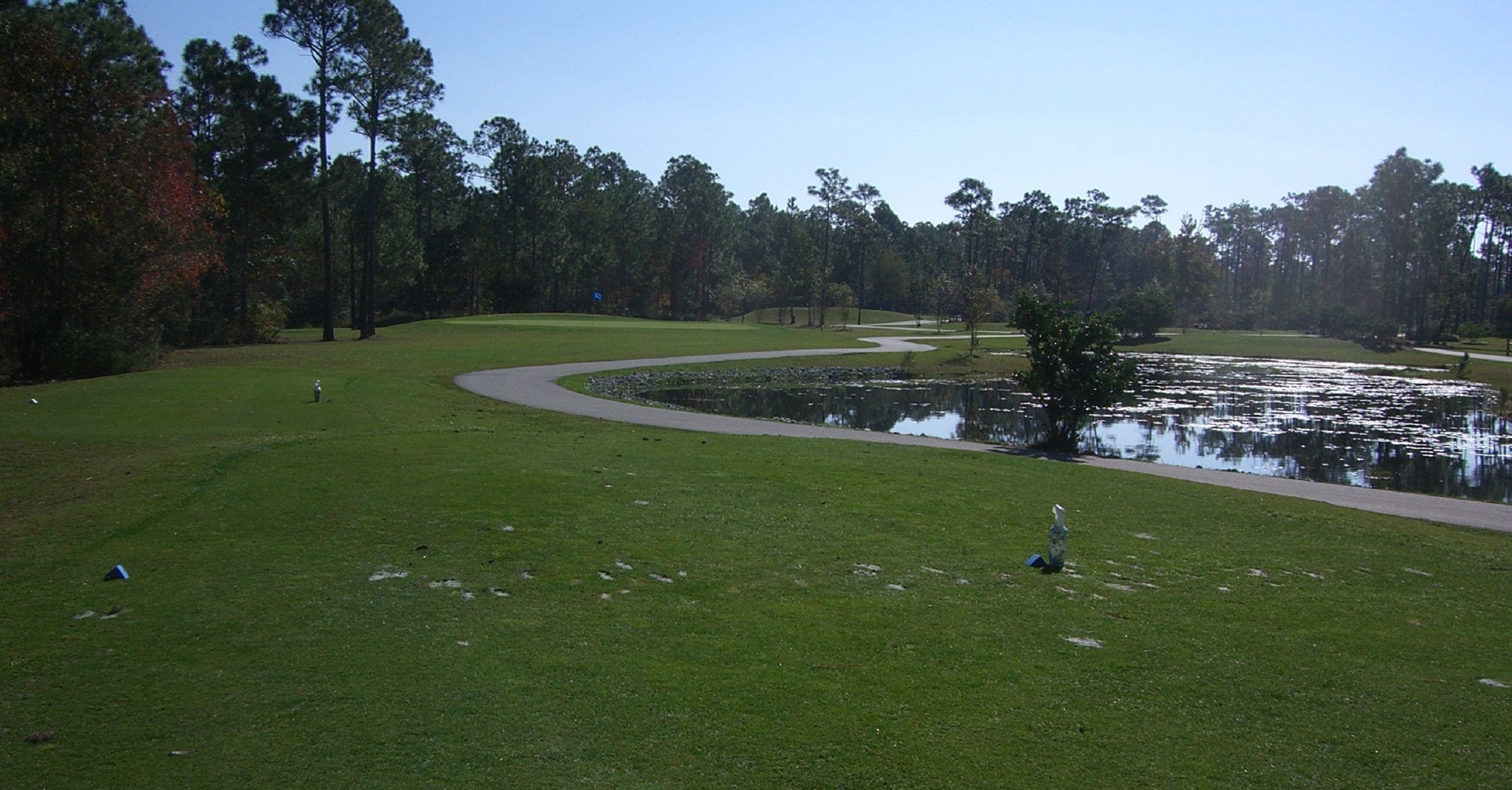 A golf course with a pond, trees, and a walking path.