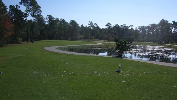 Un campo de golf con un estanque, árboles y un sendero para caminar.