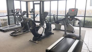 A gym with cardio machines, a treadmill, and large windows.
