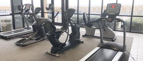 Un gimnasio con máquinas de cardio, una cinta de correr y grandes ventanales.