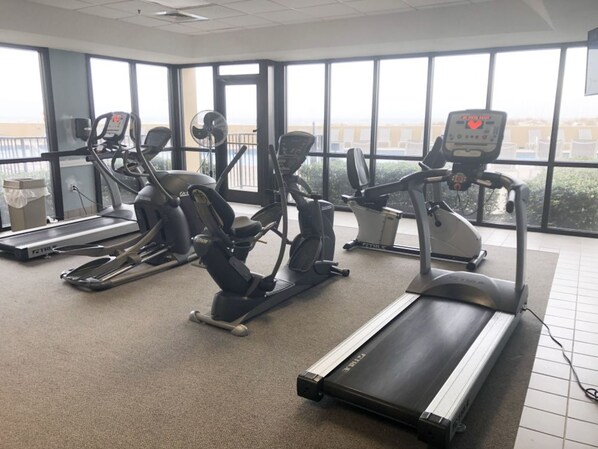 Un gimnasio con máquinas de cardio, una cinta de correr y grandes ventanales.