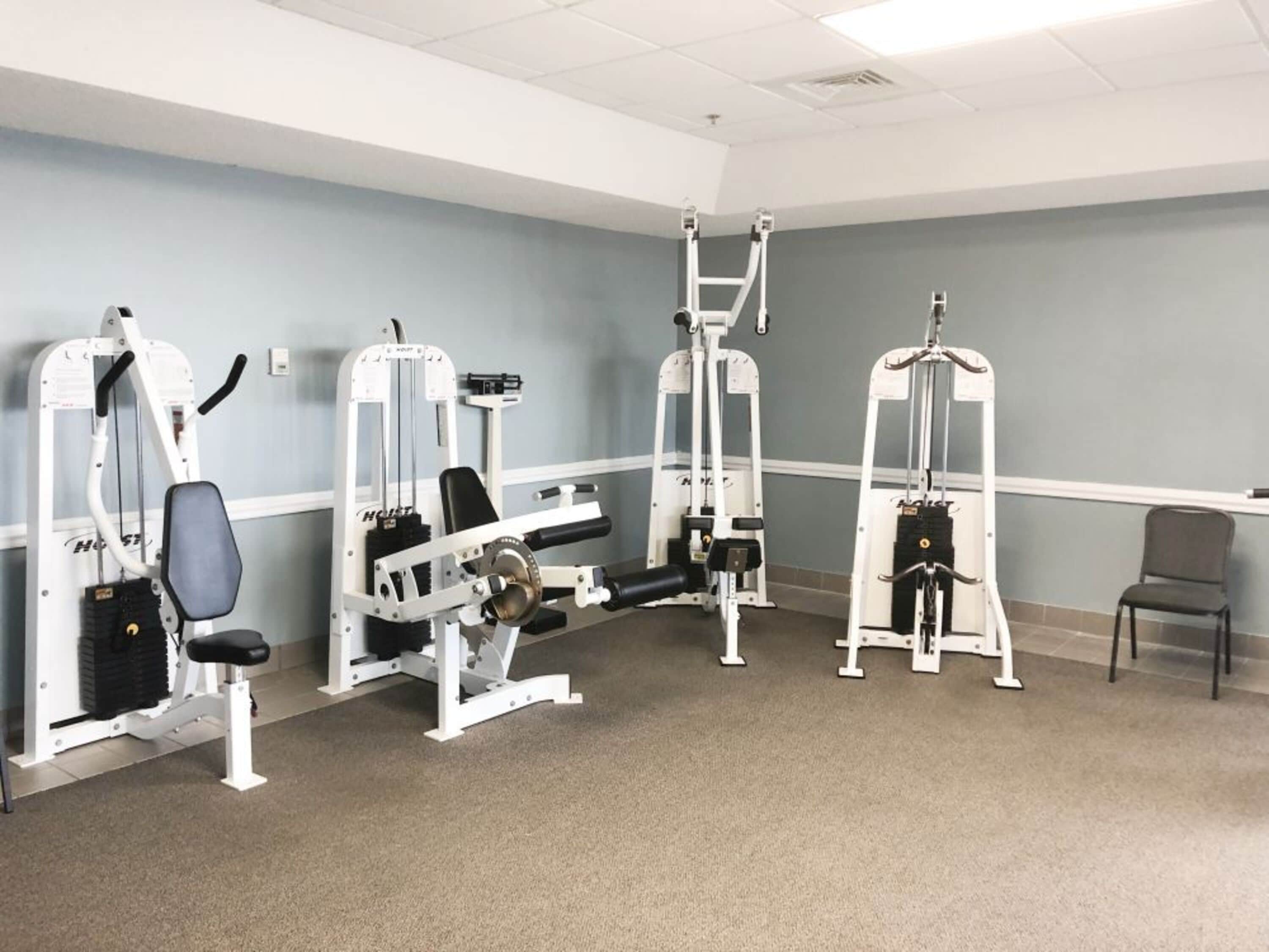 Ein Fitnessraum mit verschiedenen Trainingsgeräten, einer Bank und einem Stuhl.